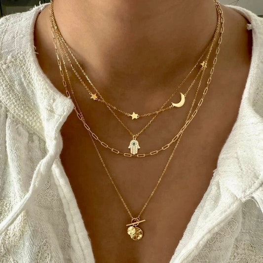 Mehrlagige goldene Kette Novashine mit Stern-, Mond- und Handanhänger am Hals, getragen zu weißer